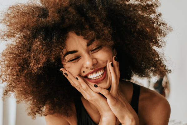 Beautiful girl with a huge smile and frizzy hair, holding her cheeks with both hands