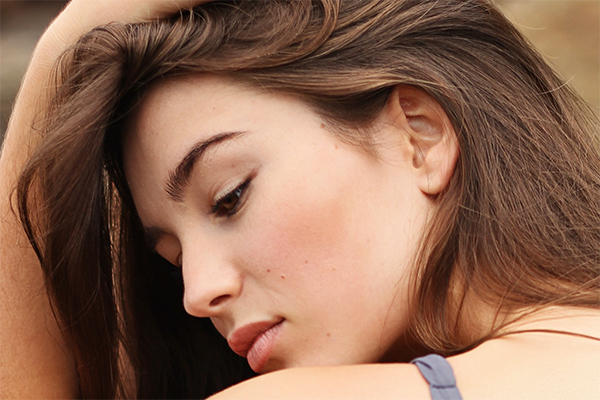 Beautiful brunette woman pushing her hair back to reveal the side of her face and ear