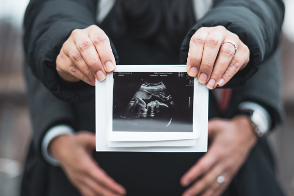 Pregnant couple. Husband holding wives stomach, while she is holding and image of of the ultrasound towards the camera.